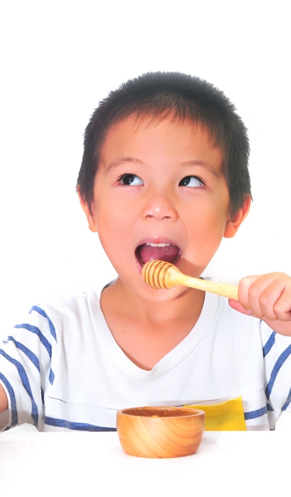 Мальчик азиат ест мед на сером фоне