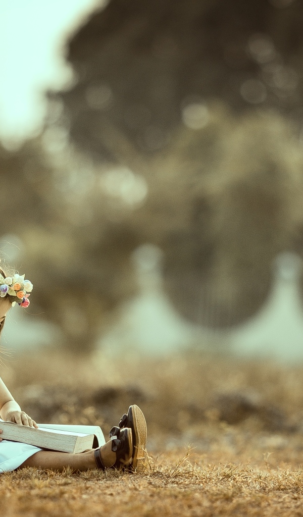 Девочка азиатка сидит с книгой на земле