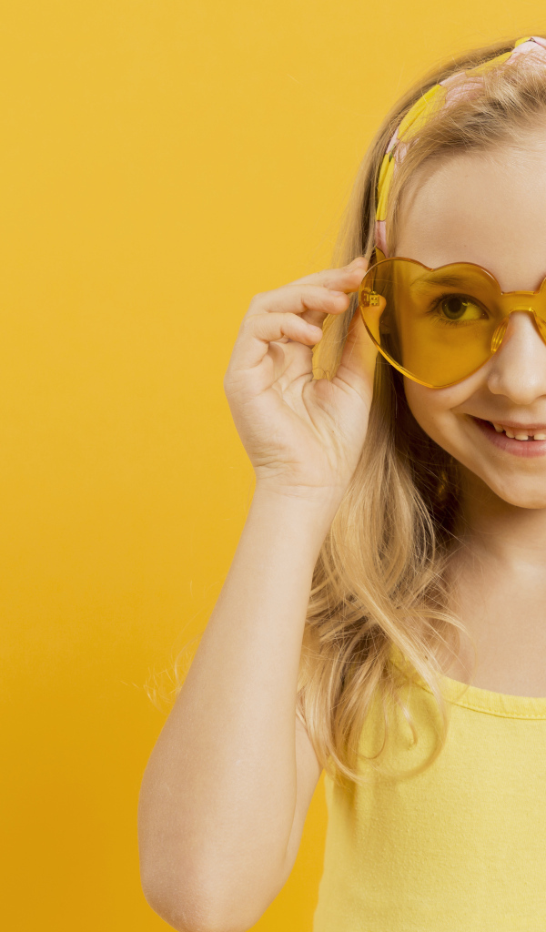 Красивая девочка блондинка в очках в форме сердца на желтом фоне