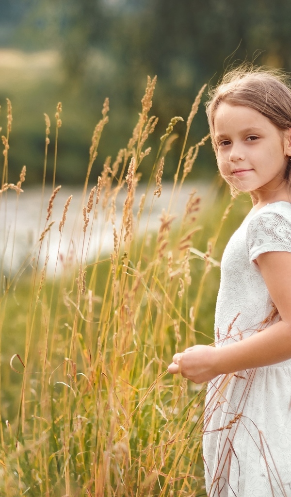 Красивая девочка в белом платье гуляет по траве