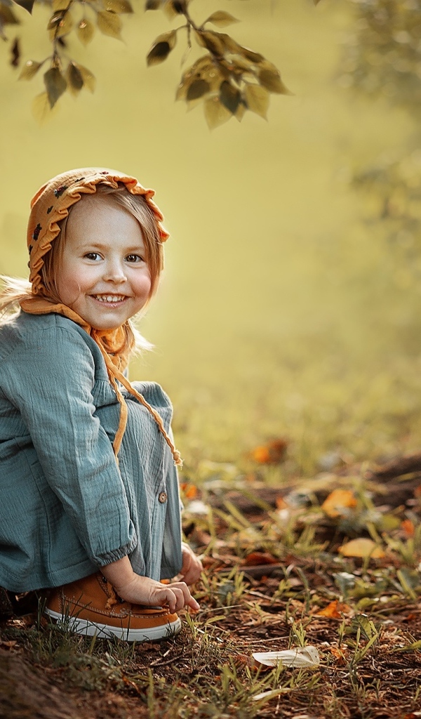 Красивая улыбающаяся девочка сидит под деревом