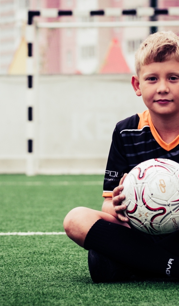 Мальчик футболист сидит на траве с мячом