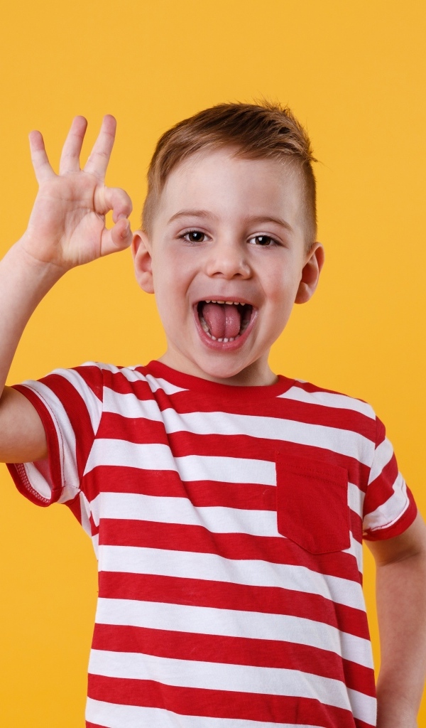 Веселый мальчик в полосатой футболке на оранжевом фоне