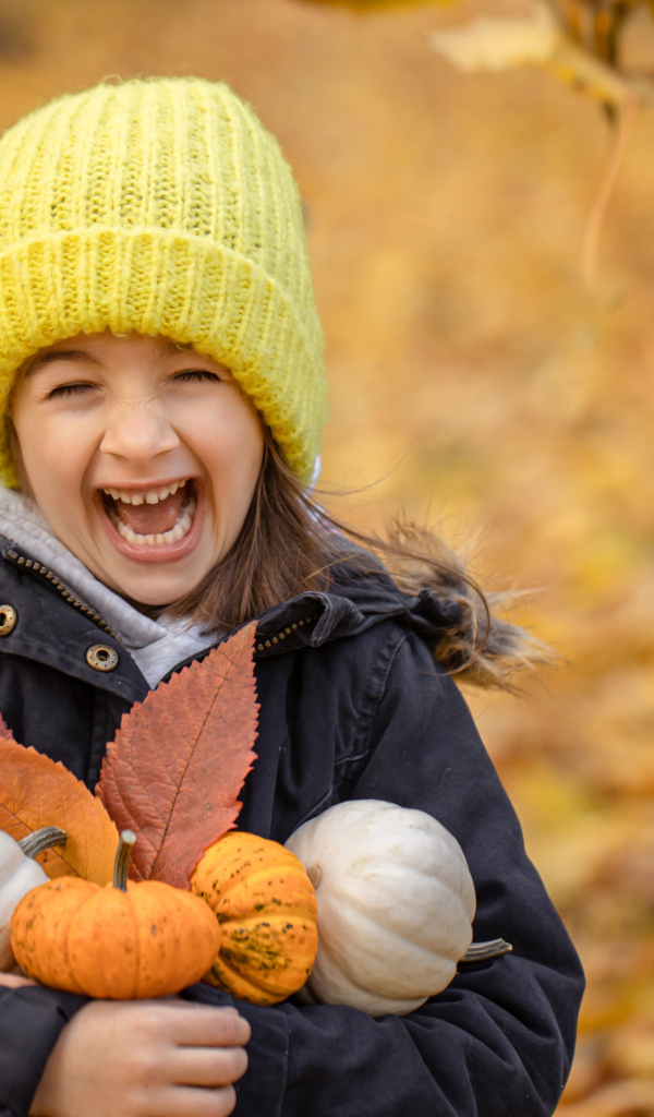 Веселая девочка с тыквами и листьями в руках осенью