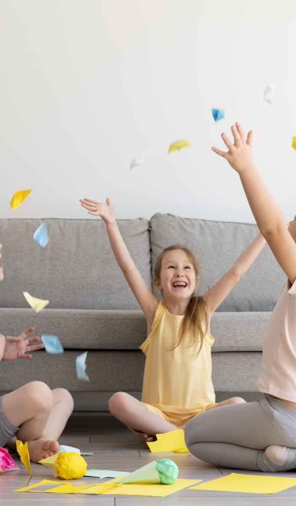 Дети играют на полу  в комнате с серым диваном