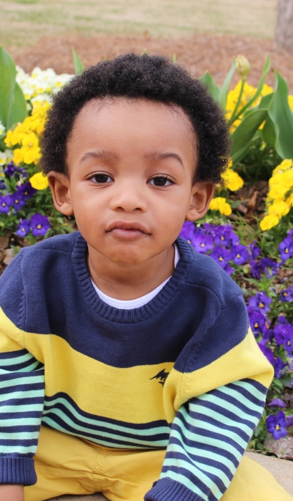 Темнокожий мальчик у клумбы с цветами 