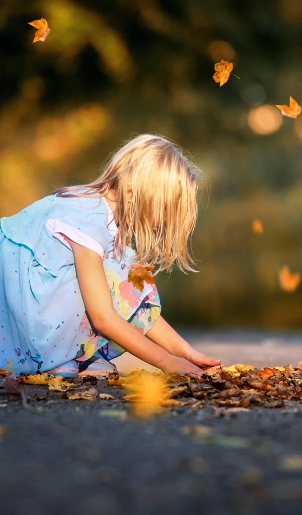 Девочка в платье играет с листьями на дороге