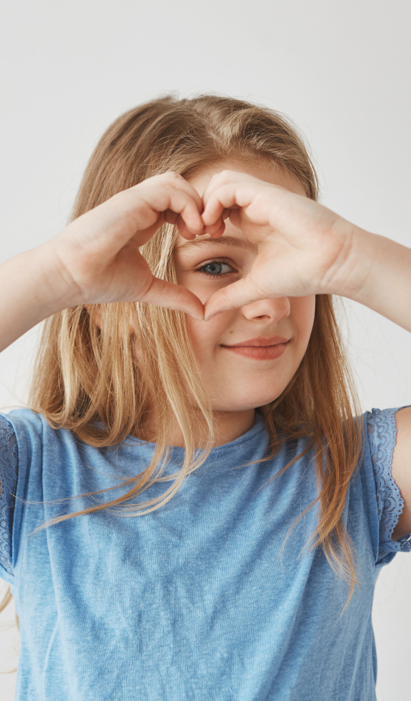 Девочка делает сердечко руками на сером фоне