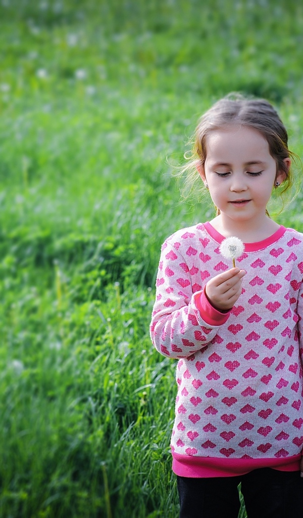 Девочка с одуванчиком на поле с зеленой травой