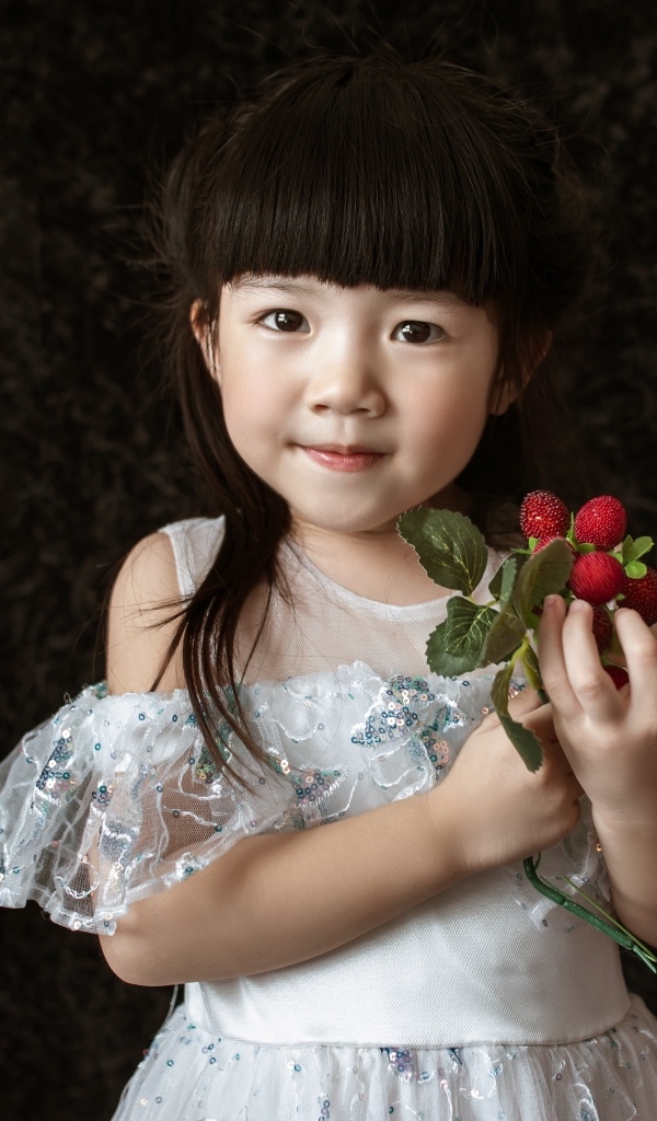 Маленькая девочка азиатка в белом платье с ягодами в руке на черном фоне