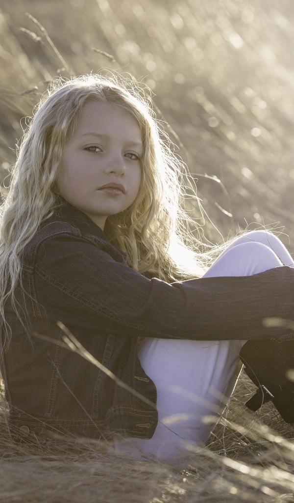 Маленькая светловолосая девочка сидит на сене