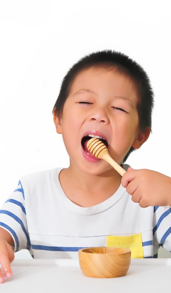 Маленький мальчик ест мед на белом фоне