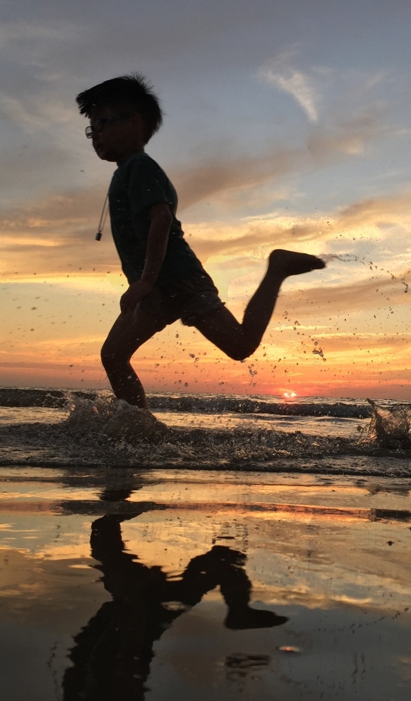 Маленький мальчик бежит по воде на закате