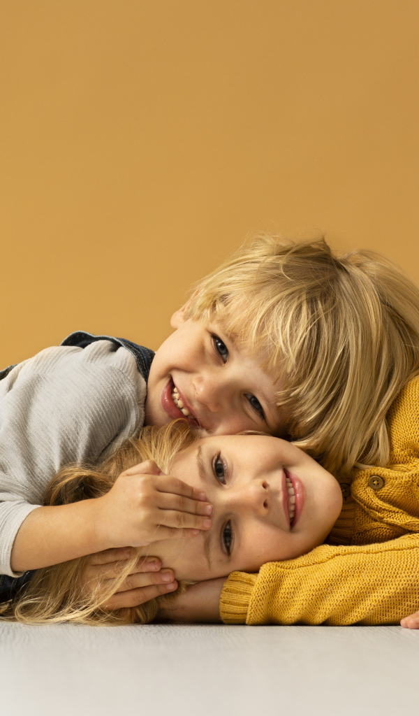 Маленькие брат и сестра лежат на полу на желтом фоне