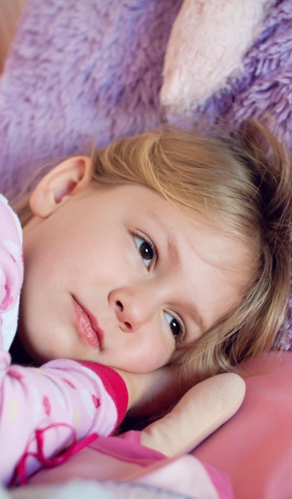 Маленькая кареглазая девочка лежит в кровати 