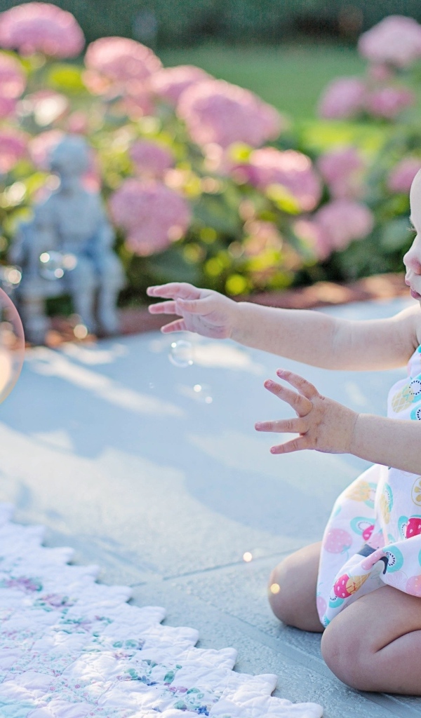 Маленькая девочка ловит мыльный пузырь на улице летом