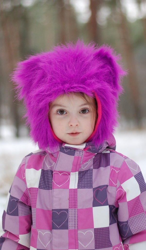 Маленькая девочка в меховой шапке в лесу зимой