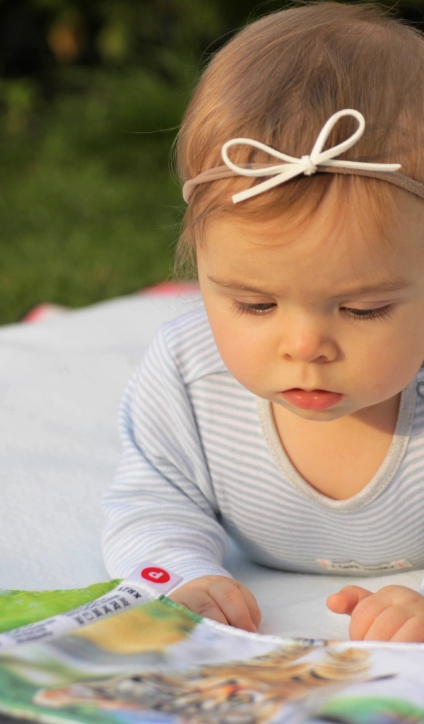 Маленькая девочка с книгой на белом покрывале