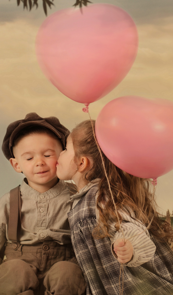 Маленькая девочка с шариками целует мальчика