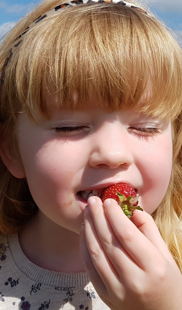 Маленькая девочка с закрытыми глазами пробует клубнику