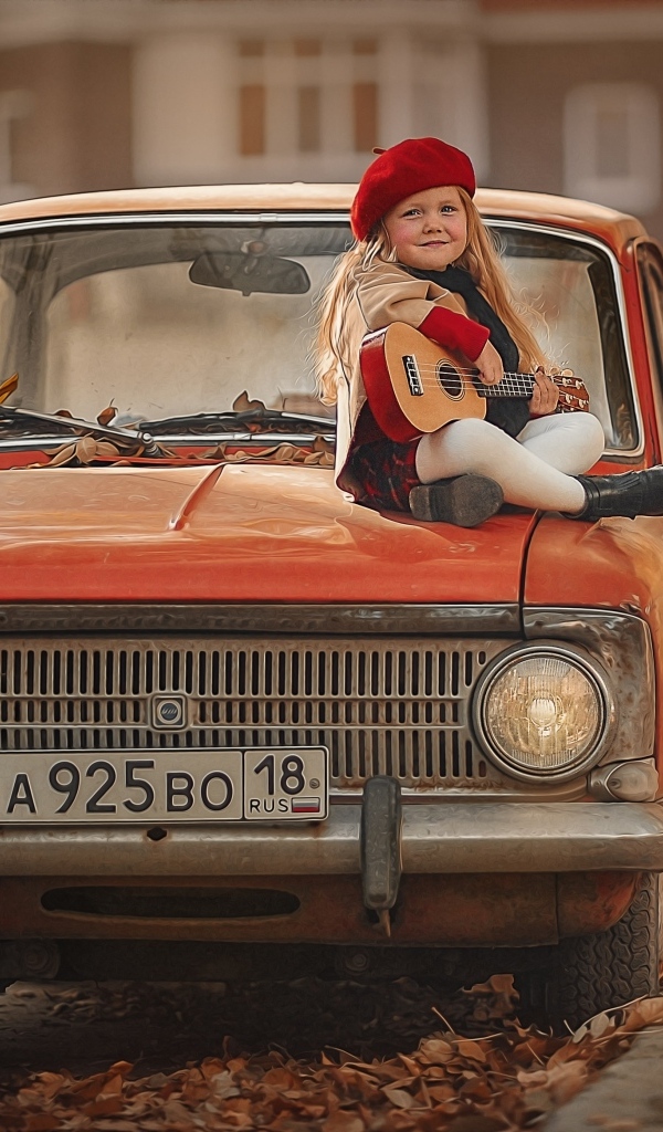 Маленькая девочка с гитарой сидит на красном автомобиле осенью
