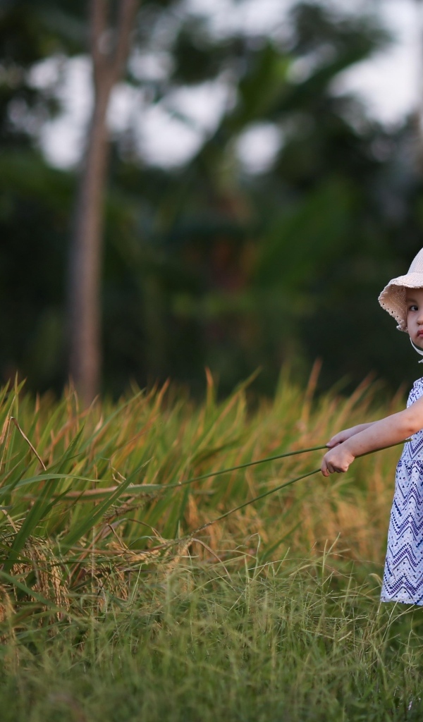 Маленькая серьезная девочка в шляпе у зеленой травы