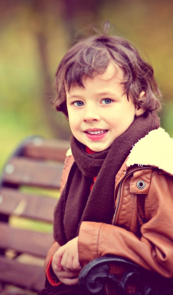 Маленький улыбающийся мальчик на лавке в парке