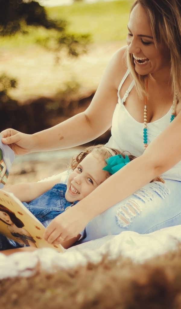 Мама читает дочери книгу на природе