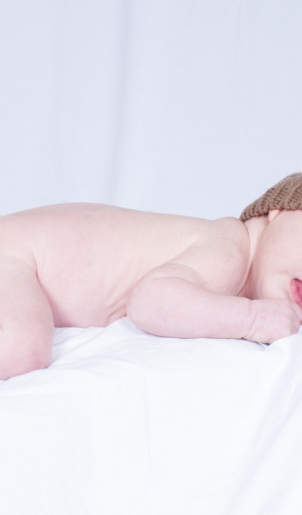 Новорожденный малыш в шапке на белой подушке