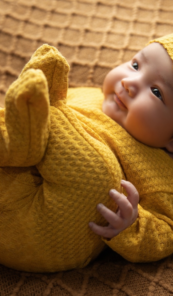 Новорожденный ребенок в желтом вязаном костюме и шапке