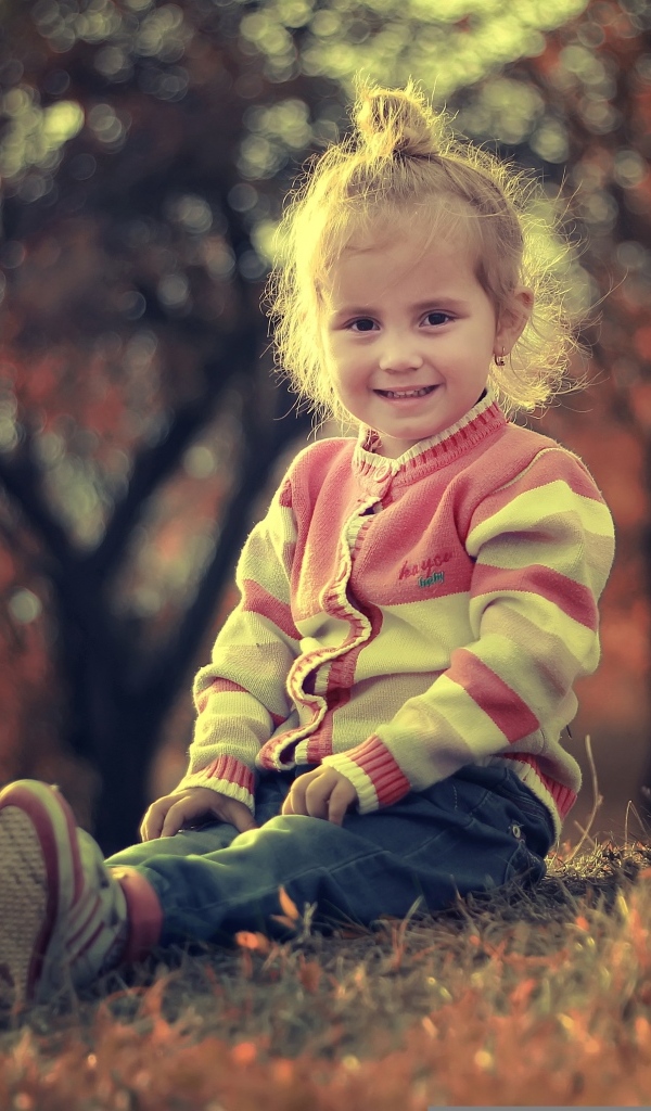 Настоящая маленькая девочка сидит на земле в лучах солнца