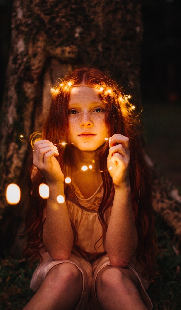 Рыжеволосая девочка с гирляндой под деревом