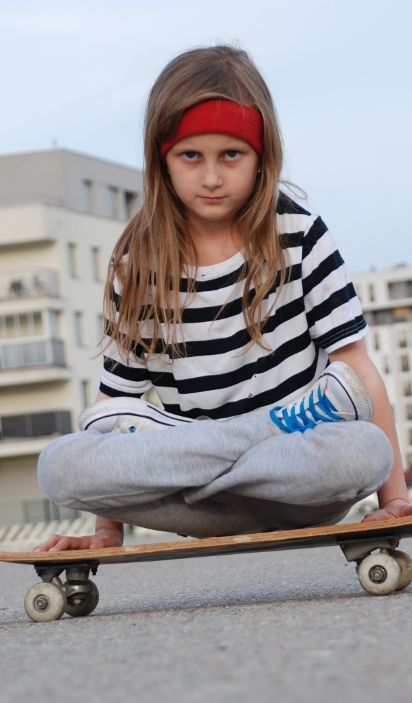 Серьезная девочка сидит на  скейтборде