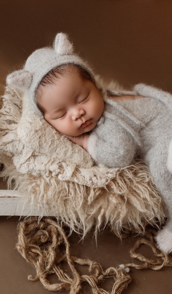 Спящий ребенок на маленькой кровати на коричневом фоне