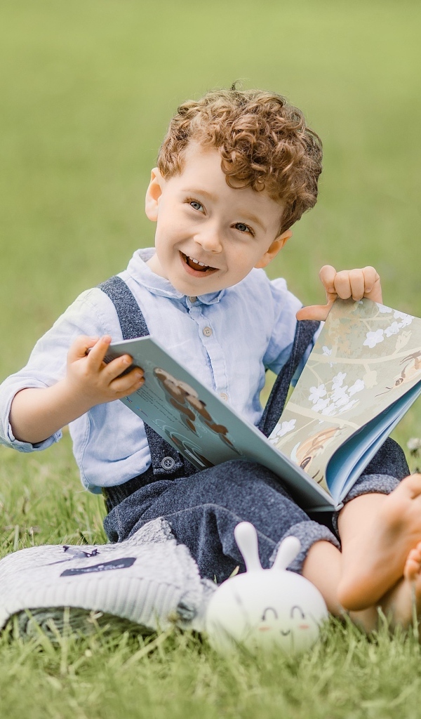 Улыбающийся мальчик с книгой сидит на траве