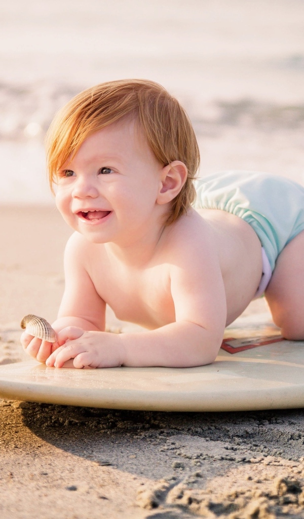 Улыбающийся ребенок с доской для серфинга на пляже