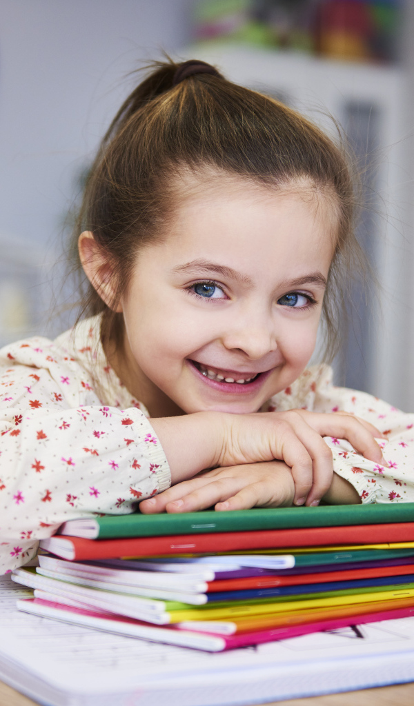 Улыбающаяся девочка ученица  с тетрадями за столом