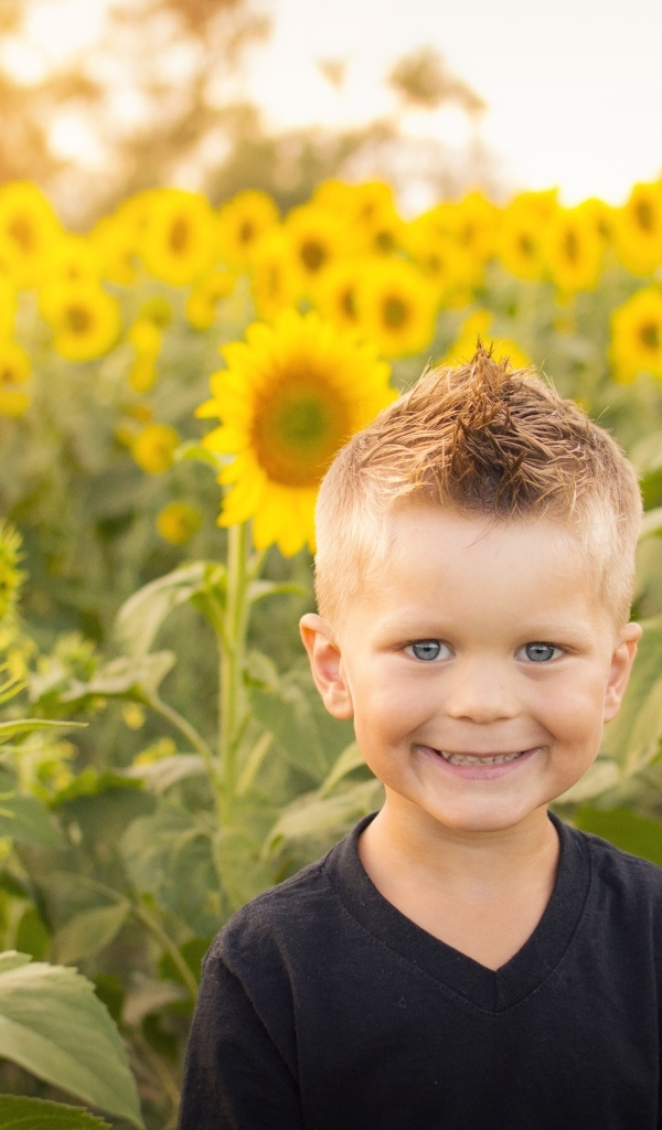 Улыбающийся маленький мальчик на поле с подсолнухами