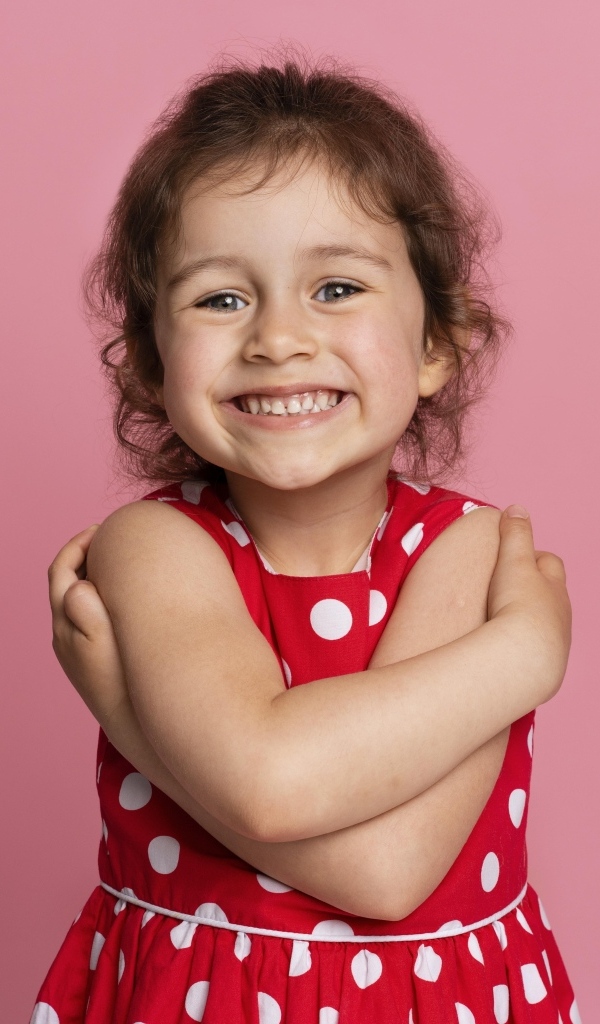 Улыбающаяся маленькая девочка в красном платье на розовом фоне