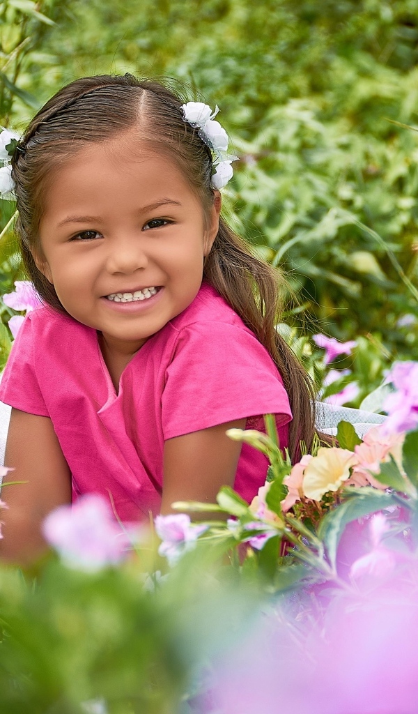 Улыбающаяся маленькая девочка сидит в цветах
