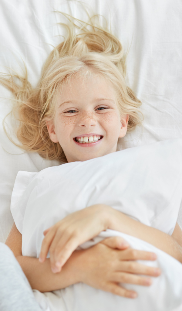 Улыбающаяся маленькая девочка с подушкой на кровати