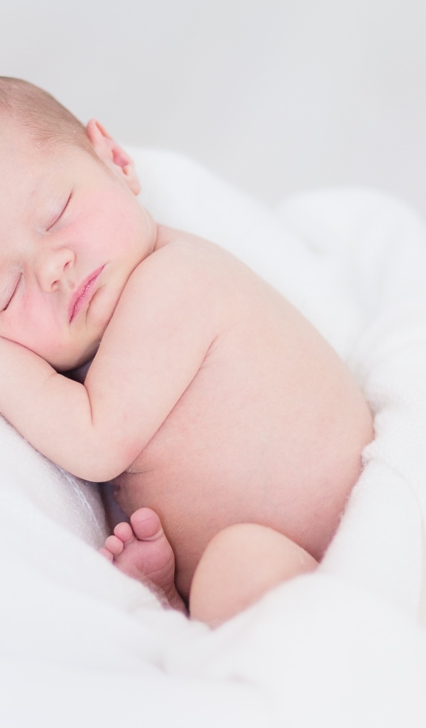 Нежный спящий новорожденный малыш на белом покрывале