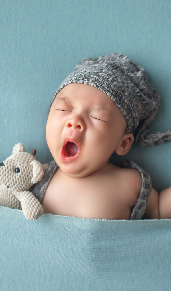 Зевающий малыш с игрушками под серым покрывалом