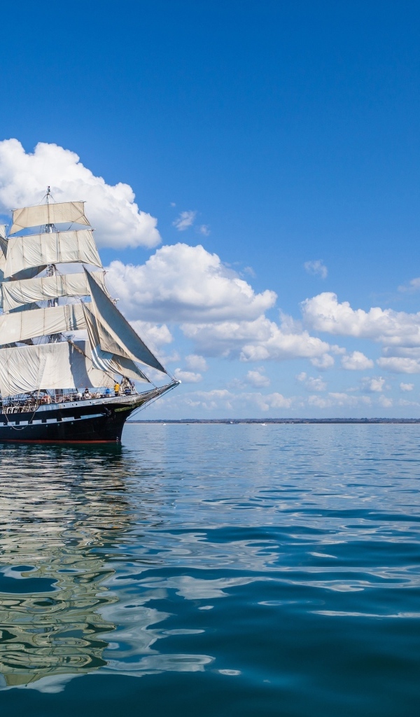 Большой корабль с белыми парусами на фоне голубого неба с облаками в море