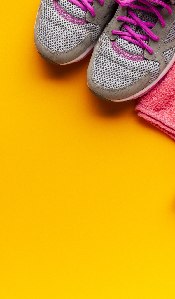 Розовые гантели, наушники, кроссовки и полотенце на желтом фоне