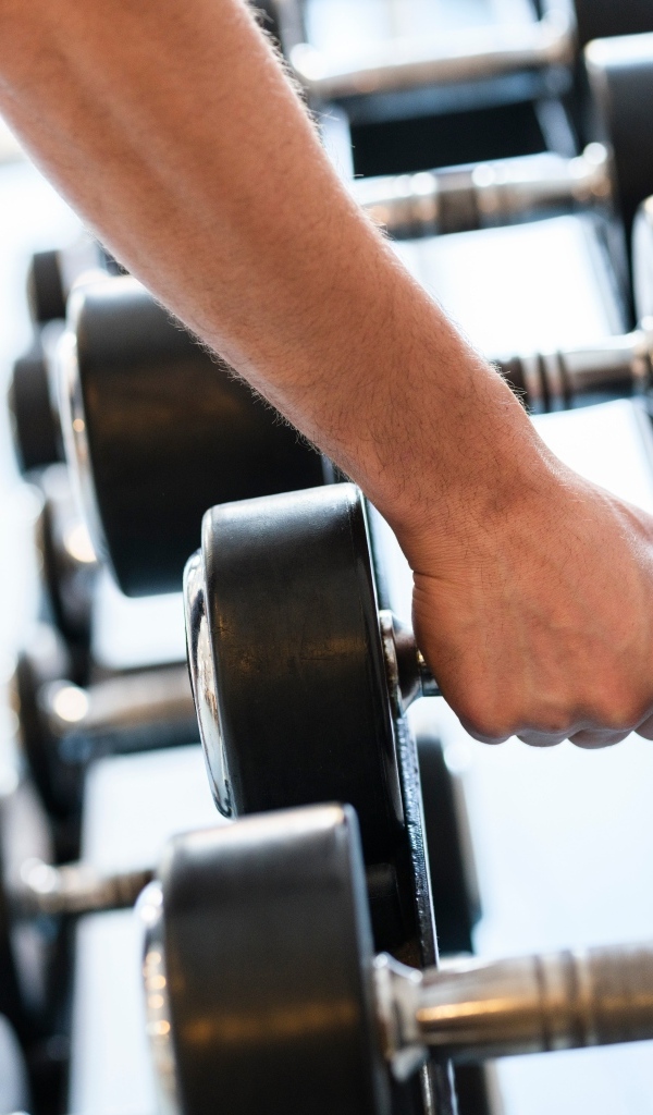 Сильная рука спортсмена берет гантели