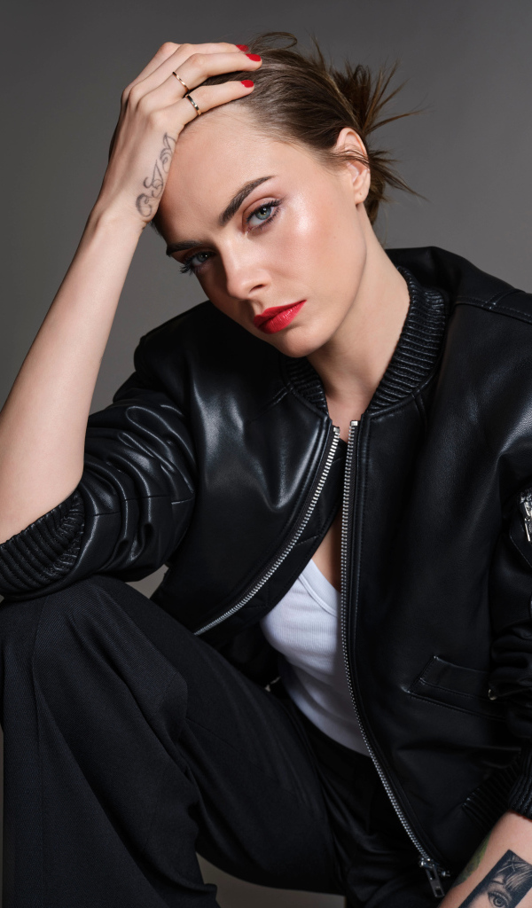 Актриса Кара Делевинь в черной кожаной куртке на сером фоне