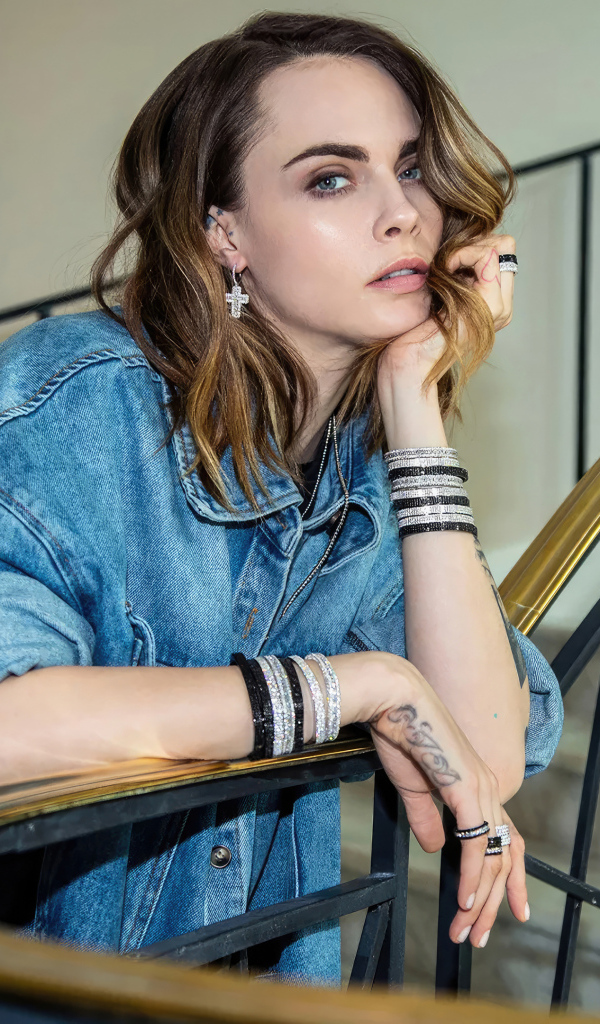 Актриса Кара Делевинь в джинсовой куртке стоит на лестнице