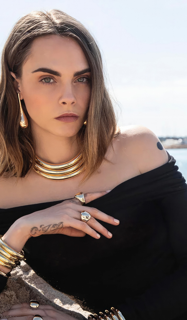 Кара Делевинь в черном платье лежит на песке