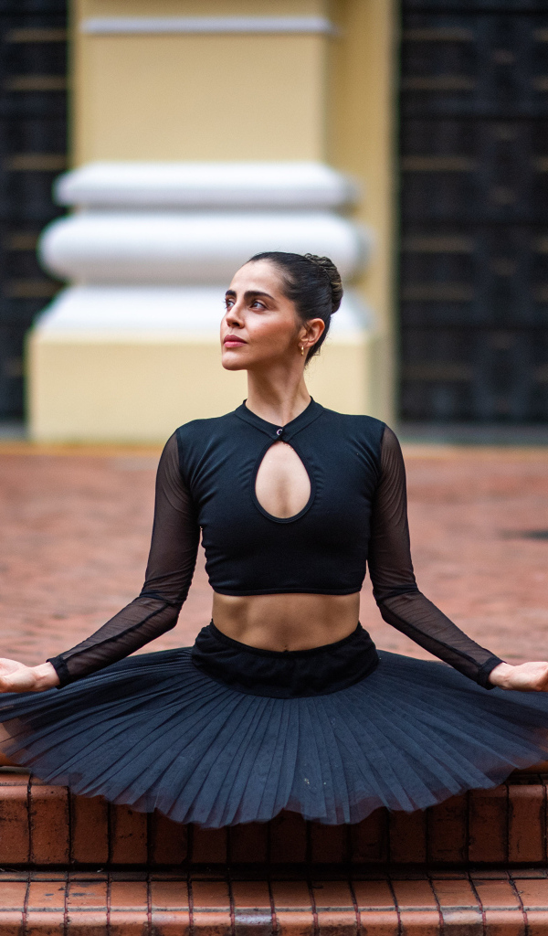 Девушка балерина в черном сидит на шпагате